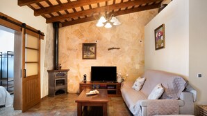 A living room with a stone wall, wooden ceiling, a sofa, a television, and a fireplace. - Holiday Home 'El Cortijo' with Private Pool, Wi-Fi and Air Conditioning (Conil de la frontera)