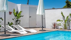 A swimming pool with lounge chairs and umbrellas, surrounded by plants and a white wall. - Holiday Home 'El Cortijo' with Private Pool, Wi-Fi and Air Conditioning (Conil de la frontera)