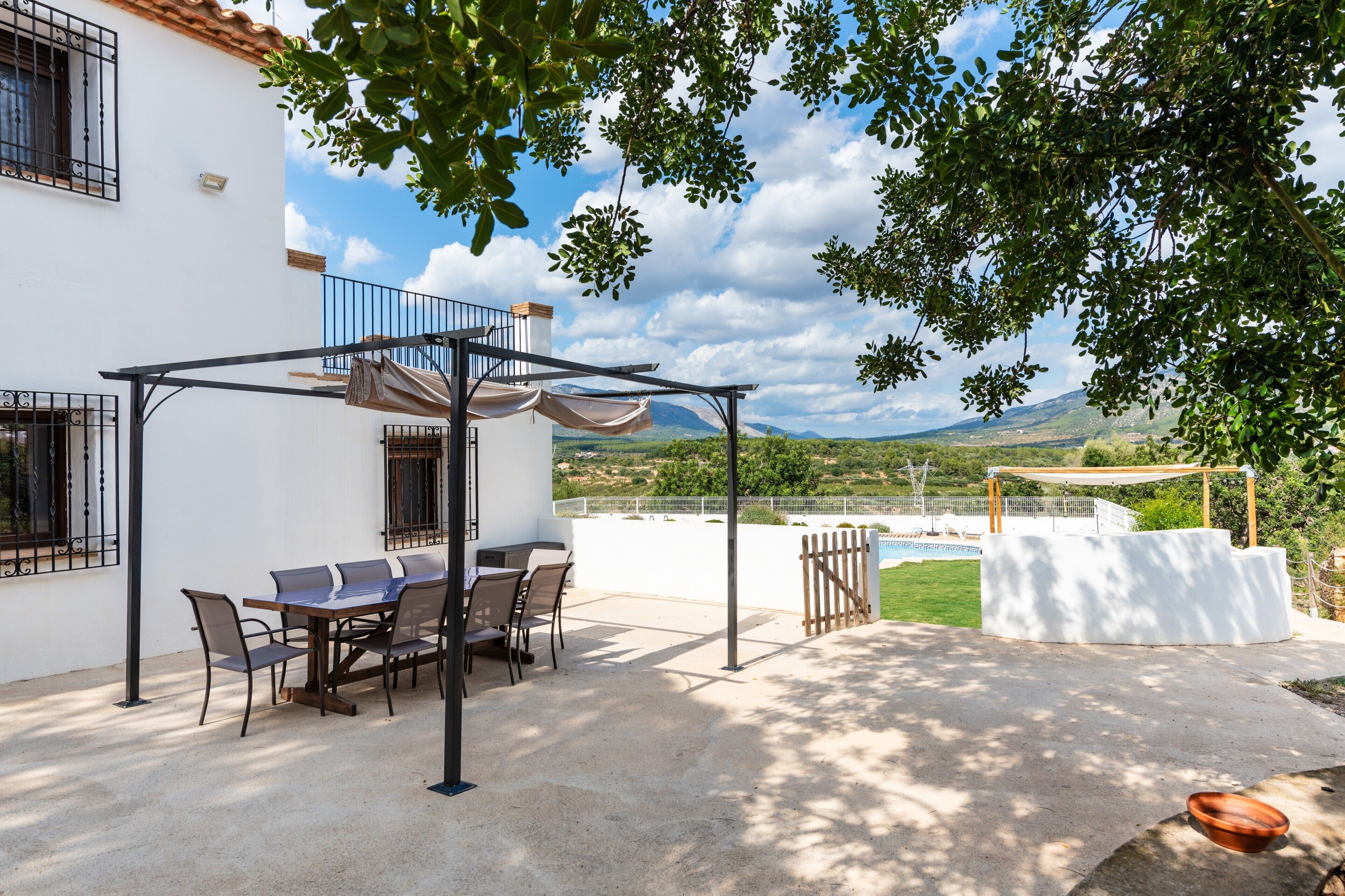 Um pátio com mesa e cadeiras, uma pérgola e vista para a paisagem.