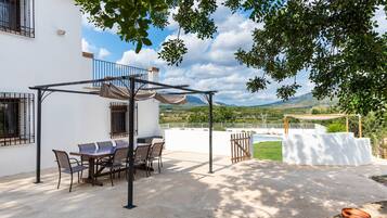 Um pátio com mesa e cadeiras, uma pérgola e vista para a paisagem.