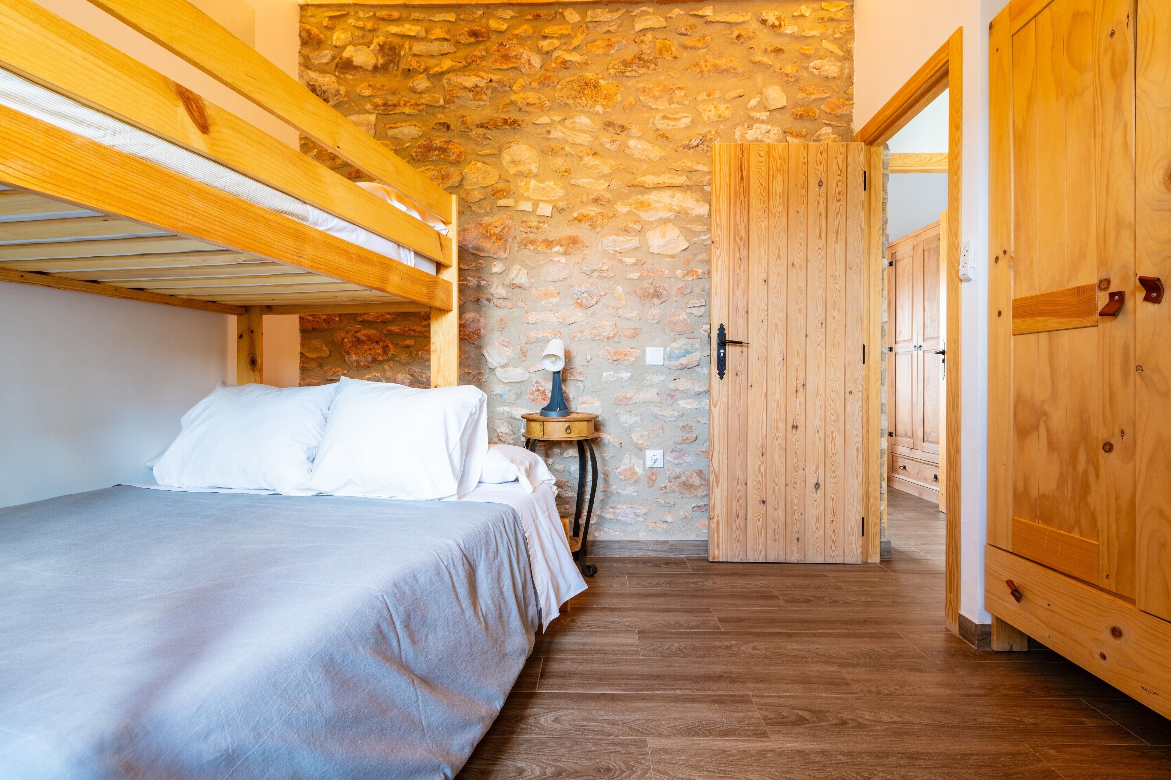 A bedroom with a bunk bed, a stone wall, wooden flooring, and a wooden wardrobe.