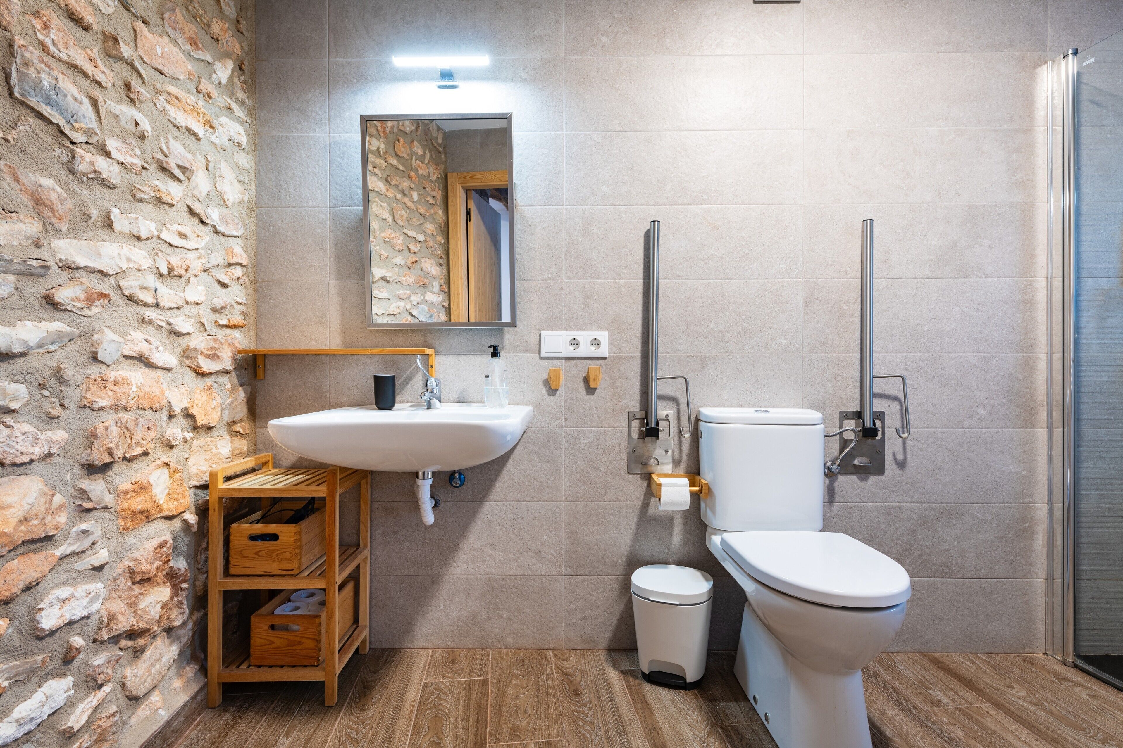A bathroom with a stone wall, a sink, a toilet, and a shower.