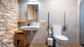 A bathroom with a stone wall, a sink, a toilet, and a shower.