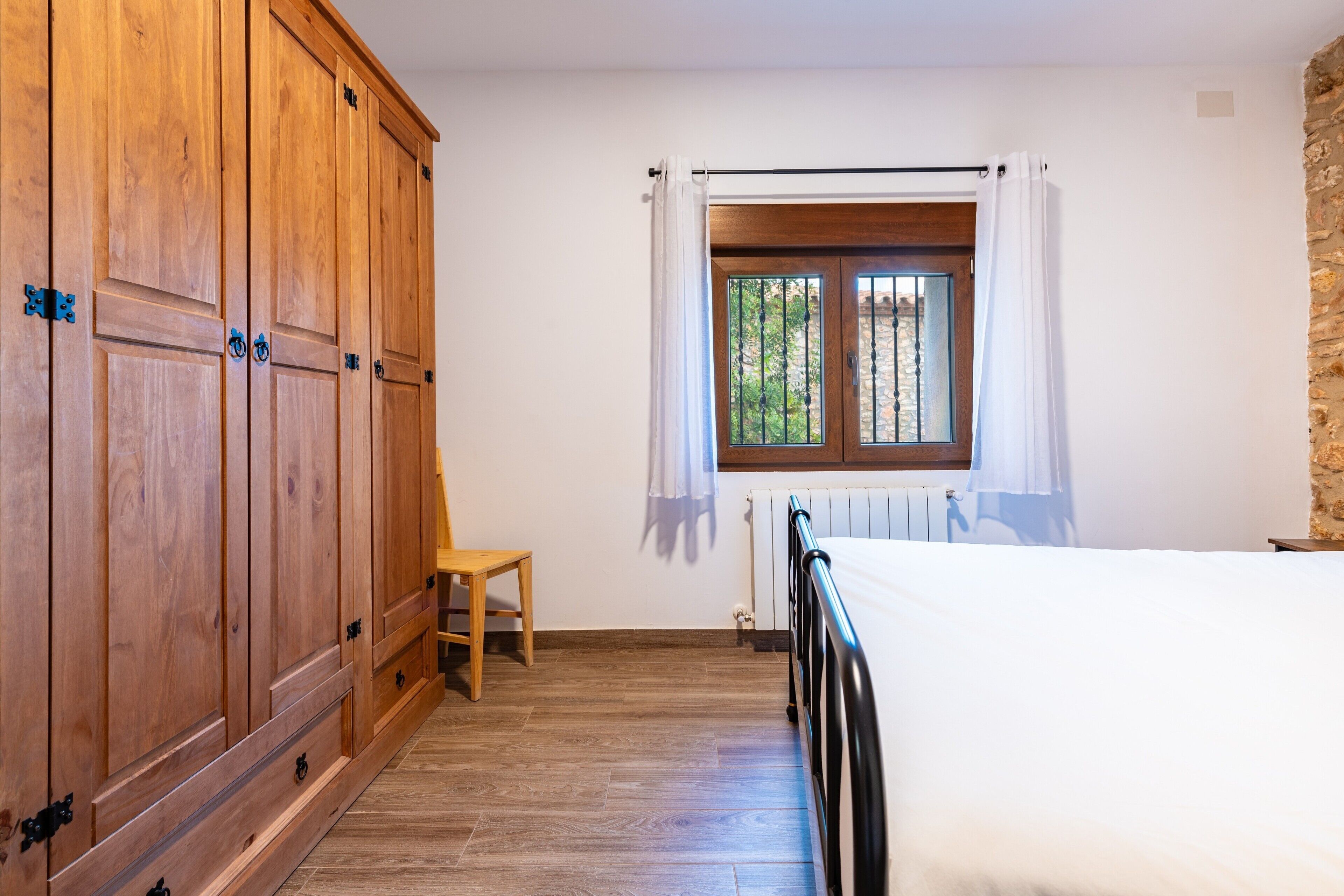 Ein Schlafzimmer mit Holzschrank, Einzelbett, Fenster mit Vorhängen und Heizkörper.