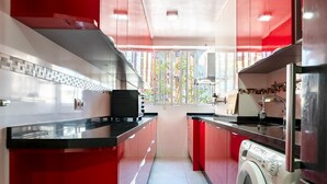 A compact kitchen with red cabinets, a washing machine, and a window providing a view of the outside. - Casa de Bella Apartment with Balcony and Wi-Fi (Fuengirola)