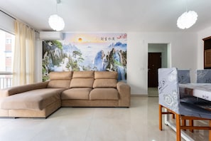 Una sala de estar con un sofá seccional, una mesa de comedor con sillas, un mural en la pared y un equipo de aire acondicionado.
