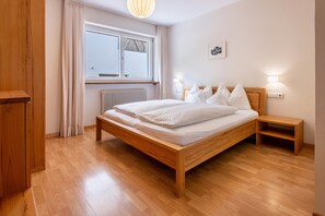 Une chambre à coucher avec un lit en bois, une table de chevet, une commode, une fenêtre avec des rideaux et un radiateur.
