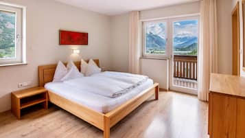 Ein Schlafzimmer mit einem hölzernen Bett, einem Nachttisch, einem Fenster mit Bergblick und einem Balkon.