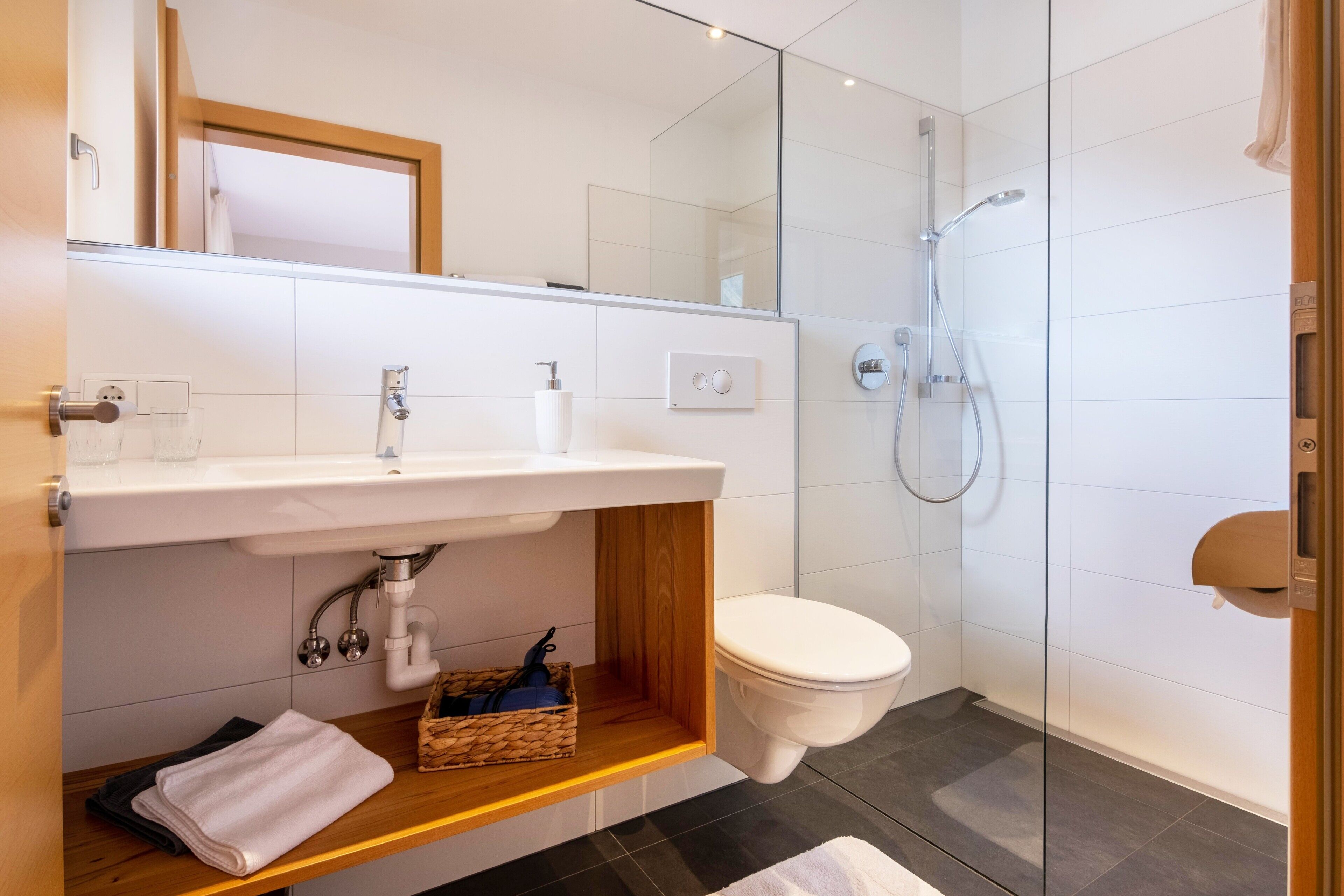 Un baño moderno con cabina de ducha de vidrio, lavamanos blanco y tocador de madera.
