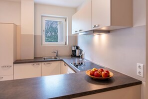 A modern kitchen with a window, stainless steel appliances, a bowl of fruit, and a coffee maker.