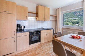 A modern kitchen with wooden cabinets, a black oven, and a dining area with a table and chairs. - Apartment 'Vermoi' with Mountain View, Shared Garden and Wi-Fi (Kastelbell)