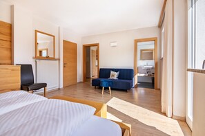 A modern hotel room with a bed, a sofa, a chair, a wooden desk, a mirror, and a view of the adjacent room. - Apartment 'Vermoi' with Mountain View, Shared Garden and Wi-Fi (Kastelbell)