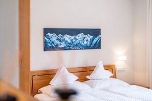 Ein Hotelzimmer mit einem hölzernen Kopfteil, zwei weißen Kissen, einem Bett mit weißer Bettwäsche, einem Wandbild von Bergen und einer Wandleuchte.