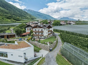 A multi-story building with balconies, surrounded by greenery and a mountainous backdrop.