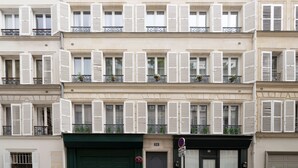 Un edificio de varios pisos con contraventanas blancas en las ventanas, balcones con barandillas y un toldo verde sobre la entrada.