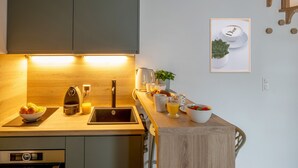 Una cocina moderna con encimera de madera, un fregadero y una tetera. Hay un bol de fruta y un vaso de jugo en la encimera.