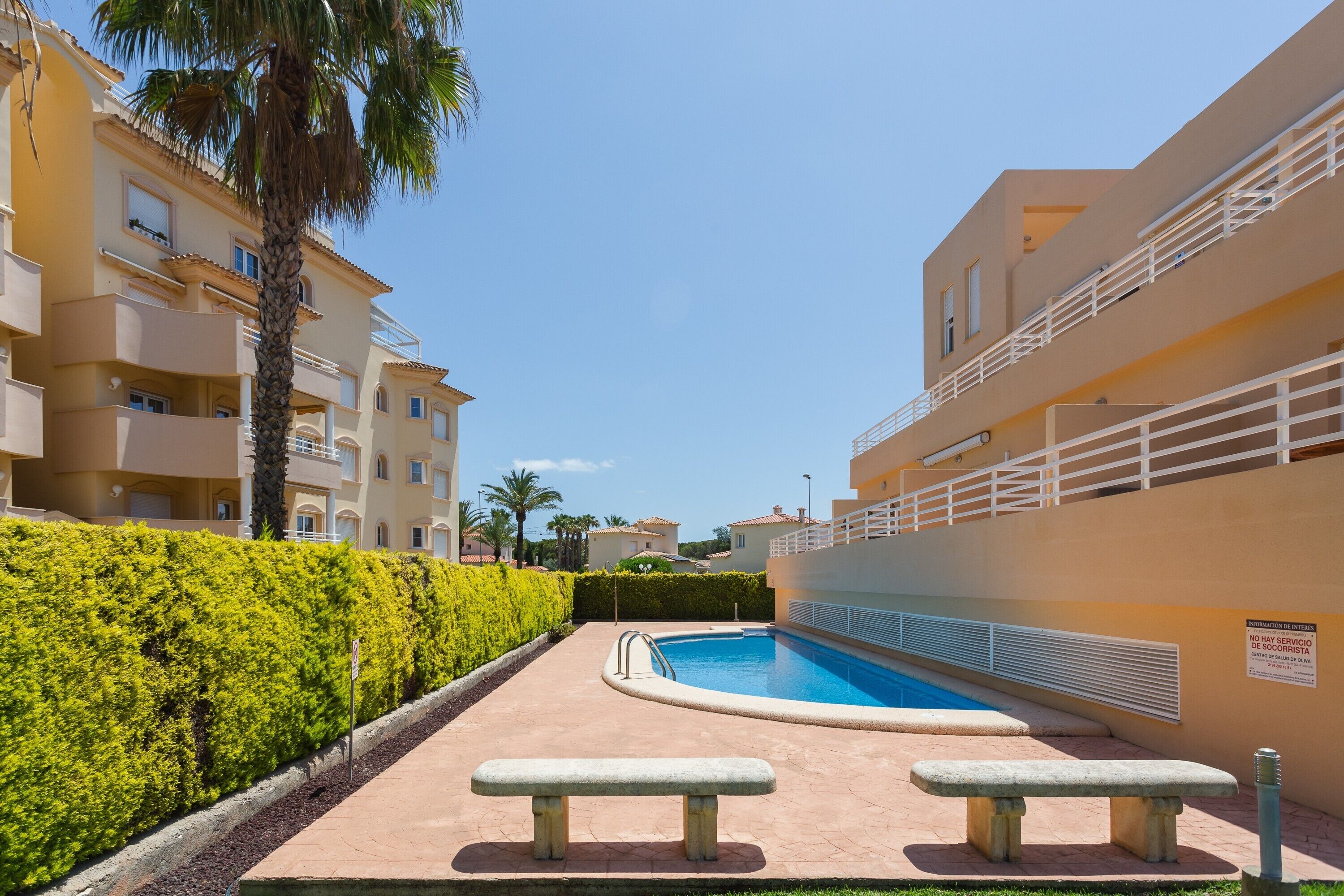 Una piscina rodeada de setos, bancos y un edificio con balcones.