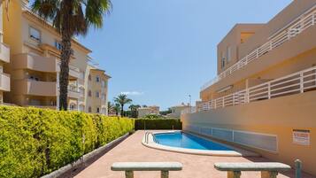 Una piscina rodeada de setos, bancos y un edificio con balcones.