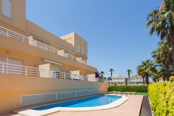 A modern hotel with a swimming pool, balconies, and palm trees.