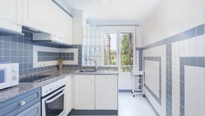 Cucina con mobili bianchi, forno a incasso, microonde e finestra con vista sugli alberi.