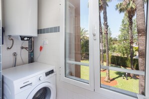 A laundry area with a Siemens washing machine, a water heater, and a window with a view of a garden. - Apartment 'Keops' with Shared Pool, Private Terrace and Air Conditioning (oliva)