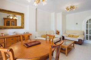 A dining area with a round wooden table, chairs, a sofa, and a coffee table. - Apartment 'Keops' with Shared Pool, Private Terrace and Air Conditioning (oliva)