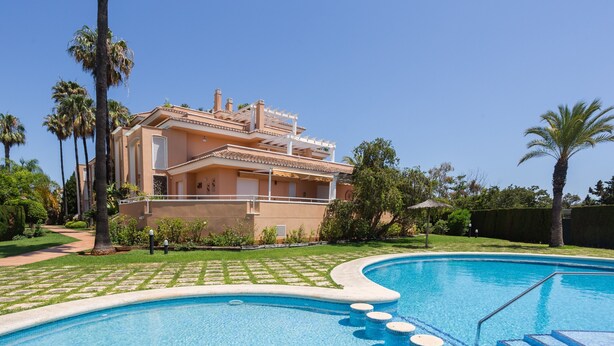 Una piscina con gradini d'accesso, circondata da un prato curato e palme.