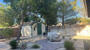 Ein Garten mit überdachter Terrasse, einem Gartenhaus und einem Holzzaun.