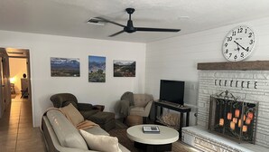 Ein Wohnzimmer mit Sofa, Sesseln, Couchtisch, Flachbildfernseher, Kamin und Bildern an der Wand.