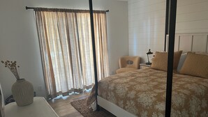 Ein Schlafzimmer mit einem Himmelbett, einem Nachttisch mit Kerzen, einem Sessel und einem Beistelltisch mit Lampe.