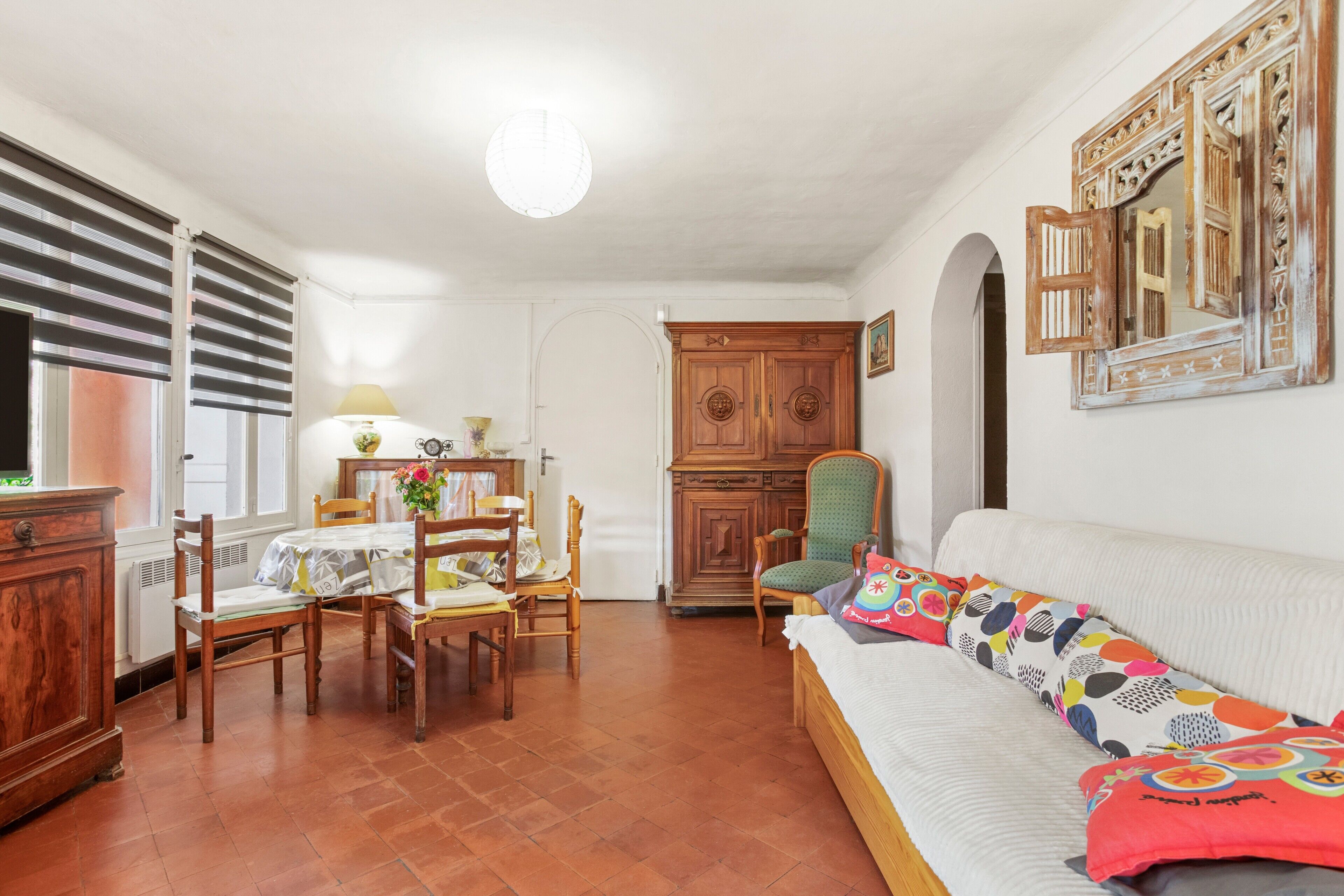 A dining area with a table and chairs, a sofa with colorful cushions, and a wooden cabinet.