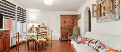 A dining area with a table and chairs, a sofa with colorful cushions, and a wooden cabinet.