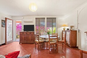 Uma sala de jantar com uma mesa redonda, cadeiras, uma televisão e um armário.