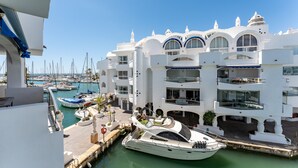 Una marina con varios yates amarrados, un edificio blanco con balcones y un cielo azul despejado.