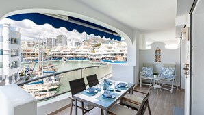 Un balcón con mesa, sillas y vista a un puerto deportivo con barcos y edificios.