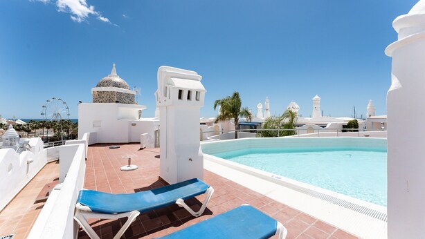 Un área de piscina en la azotea con sillones reclinables azules y vistas despejadas al océano.
