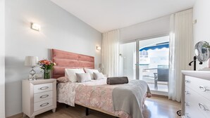 Un dormitorio con cama, mesita de noche, lámpara y vistas al exterior.