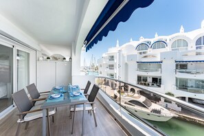 Un balcon équipé d’une table à manger, de chaises et offrant une vue sur une marina avec des bateaux et des bâtiments.