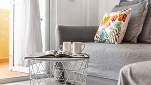 Un salón acogedor con un sofá gris, un cojín estampado y una mesita con dos tazas blancas y una revista abierta.