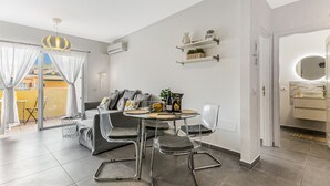Una sala de estar moderna con un sofá, dos sillones, una mesa redonda y un balcón con cortinas.