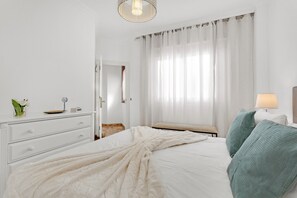 Ett hotellrum med en säng, ett nattduksbord, en lampa, ett fönster med gardiner och en dörr.