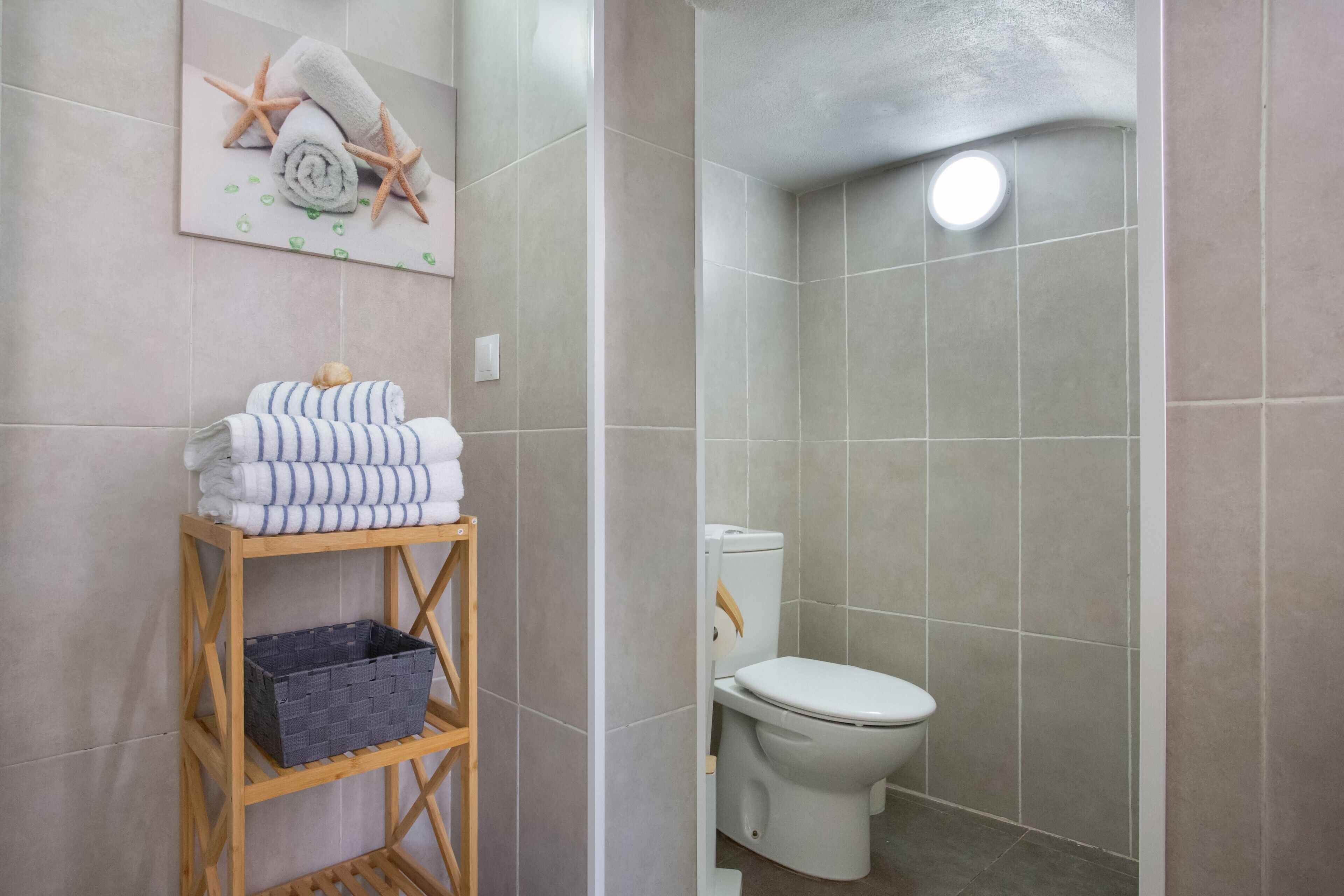 Een badkamer met een toilet, een douche, een houten plank met handdoeken en een aan de muur hangend schilderij.