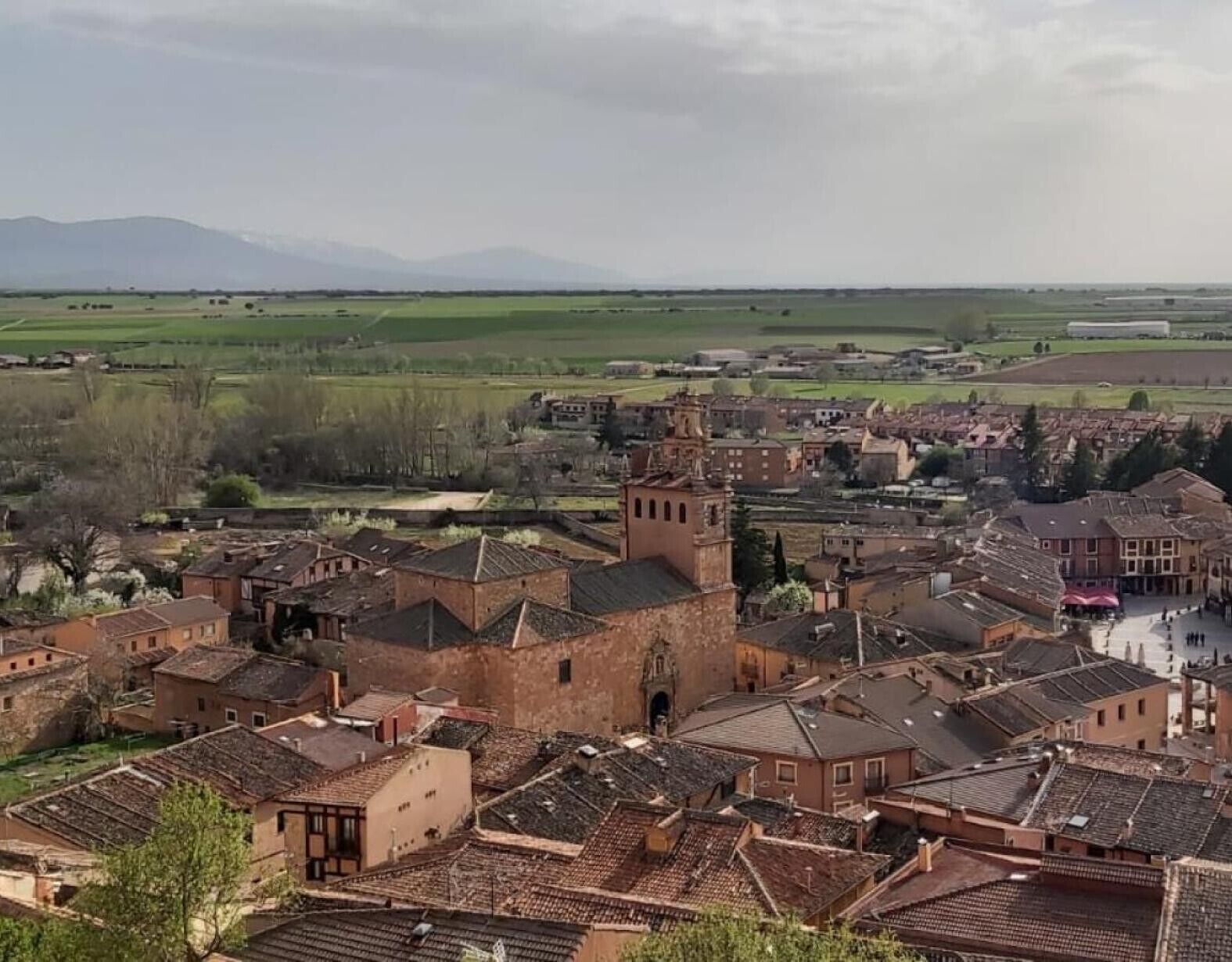 Uma cidade histórica com arquitetura tradicional, incluindo uma torre imponente, e uma paisagem rural ao redor.
