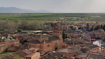 Uma cidade histórica com arquitetura tradicional, incluindo uma torre imponente, e uma paisagem rural ao redor.