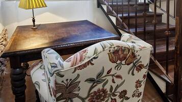A dining table with a lamp, a floral-patterned chair, a staircase, and a bookshelf in the background.