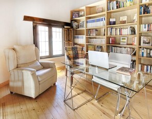 A living room with a glass table, a sofa, a chair, and a bookshelf filled with books.