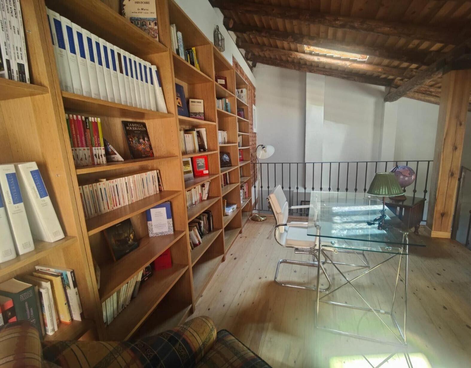 Habitació amb prestatgeries de fusta plenes de llibres, una taula de vidre, una cadira i una làmpada.