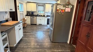 A kitchen with white cabinets, a stainless steel refrigerator, and a wooden floor. - Maple Creek Retreat (Owatonna)