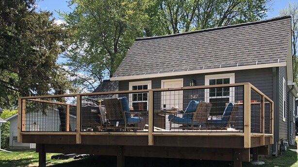 A house with a wooden deck, a fenced patio area, and a large tree in the background. - Maple Creek Retreat (Owatonna)
