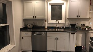 A kitchen with white cabinets, a stainless steel sink, and a window above the sink. - Maple Creek Retreat (Owatonna)
